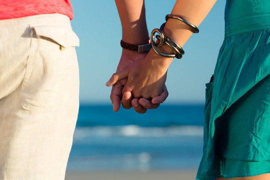 男人和女人，情侣，在度假时在海边的海滩上享受浪漫的日落，他们手拉手站在一起，特写镜头
