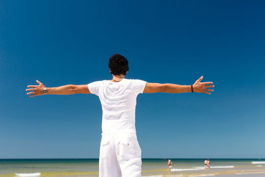 海边的帅哥在享受暑假，双臂伸向阳光象征着自由