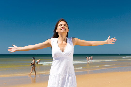美丽的女人在海边享受着她的暑假，双臂伸向太阳象征着自由