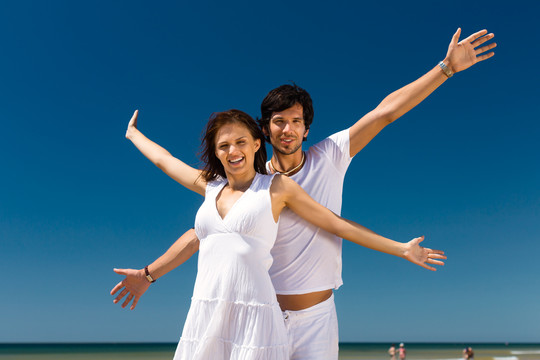 一对年轻的情侣在海边享受他们的暑假，双臂伸向阳光，象征着自由