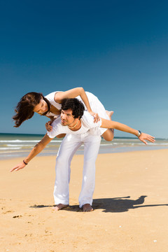 一对嬉戏的情侣在海边享受暑假，男人背着女人