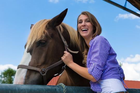 马厩里的年轻女子，带着马在阳光下微笑