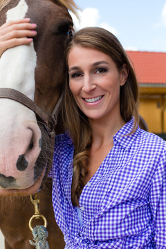 马厩里的年轻女子，在阳光下微笑着牵着马