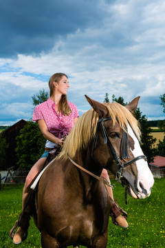 在多云的天空下，年轻女子在草地上骑马