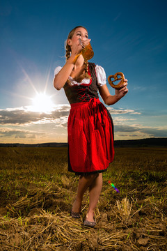 年轻的巴伐利亚女子喝着啤酒，手里拿着一个椒盐卷饼