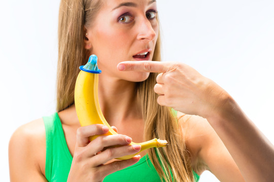 年轻女子在白色背景下展示带蓝色避孕套的香蕉的特写镜头