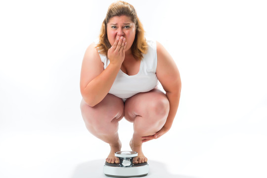 饮食和体重，肥胖的年轻女子蹲在秤上测量她的体重