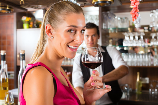 在宾馆或饭店的酒吧里，一个女人手里拿着一杯红酒，面带微笑