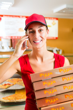 在一家披萨店当送货员的女人，手里拿着几个披萨盒，面带微笑