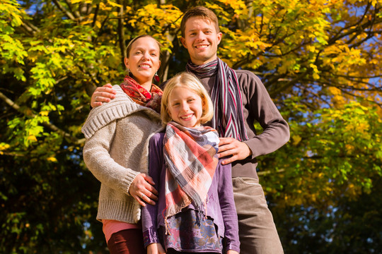 幸福的家庭，母亲，父亲和女儿或孩子坐在户外的草地上与五颜六色的叶子和树下，在秋天或秋天