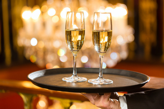 服务员在一家高级餐厅的托盘上端上香槟酒杯，背景是一盏大吊灯