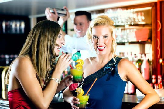 年轻女子在酒吧或俱乐部喝鸡尾酒时，酒保正在调酒