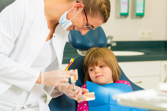 外科牙医拿着假牙，用牙刷向一个儿童患者解释