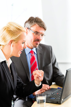 商务-两位身着商务装的专业人士在办公室里看着笔记本电脑屏幕一起工作