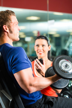 男子或健美运动员与私人健身教练在健身房练习哑铃运动，特写
