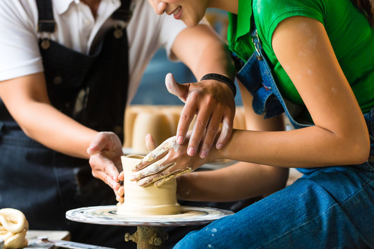 女陶工在陶工的轮子上制作一个碗，陶工师傅在帮她