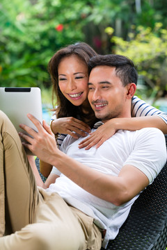 印尼一对年轻夫妇——一男一女——坐在花园里，手里拿着一台平板电脑