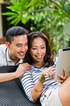印尼一对年轻夫妇——一男一女——坐在花园里，手里拿着一台平板电脑