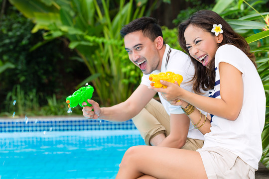年轻的印尼夫妇-男人和女人-在花园游泳池在热带环境下，你玩水枪