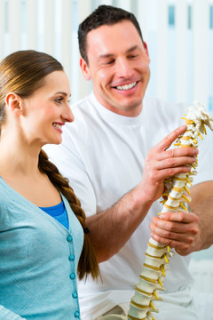 理疗师在他的实践中，他向一名女性患者解释了脊柱和背痛的出现