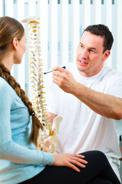 理疗师在他的实践中，他向一名女性患者解释了脊柱和背痛的出现