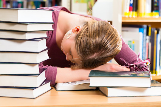 女学生在图书馆看书学习，她睡着了，又累又累