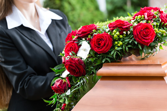 葬礼上站在棺材或棺材前的红玫瑰的哀悼妇女