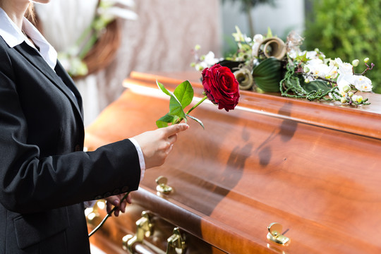 葬礼上站在棺材或棺材前的红玫瑰的哀悼妇女