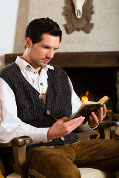 年轻人在传统的带壁炉的山间小屋里读圣经