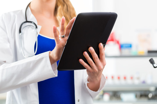 年轻的女医生站在诊所里用平板电脑阅读文件或档案