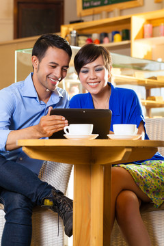 亚洲朋友在咖啡馆里享受她的闲暇时光，喝咖啡或卡布奇诺，在平板电脑上看照片或电子邮件