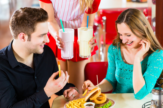 在美式快餐店，朋友或情侣在吧台上吃快餐，喝奶昔，女服务员穿着短装
