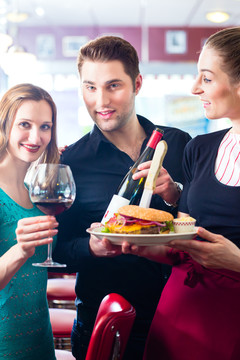 在美式快餐店吃快餐的朋友或夫妇，服务员提供食物、汉堡、薯条和红酒