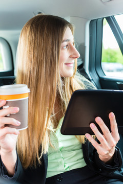 坐出租车旅行的年轻女商人，她手里拿着一杯咖啡和一台平板电脑