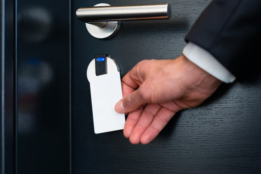 酒店门-一个年轻人拿着钥匙卡在一个房间门的电子传感器前