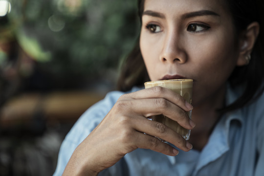 特写亚泰妇女在咖啡馆喝咖啡拿铁从玻璃杯。