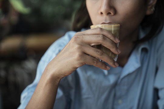 特写亚泰妇女在咖啡馆喝咖啡拿铁从玻璃杯。