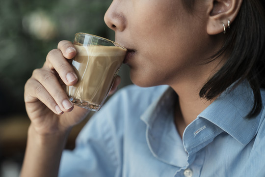侧视特写亚泰妇女在咖啡厅喝咖啡拿铁从玻璃杯。