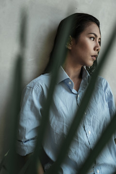 身着蓝色连衣裙的泰国亚裔女子站在前景绿叶的阁楼墙上。