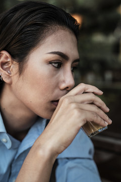 脸部特写身着蓝色连衣裙的亚泰妇女用右手喝咖啡。