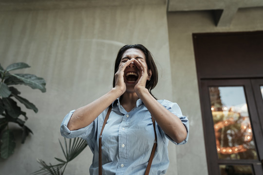 身着蓝色连衣裙的亚泰女子在街上用手捂住嘴大声喊叫。