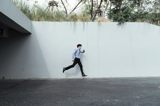 身着正装的亚洲年轻人在白色墙壁背景上奔跑。