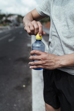 运动员年轻人跑累后打开一瓶水。