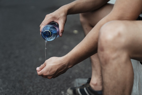 坐在路边的一个运动男子从瓶子里倒水来洗手。