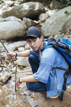 男性徒步旅行者在森林里有大石头的瀑布边休息。