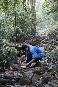 坐在森林小路上系鞋带的男性徒步旅行者。