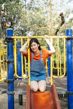 长发女孩穿着橙色t恤和牛仔裤套头衫坐在操场滑道顶端的膝盖上。