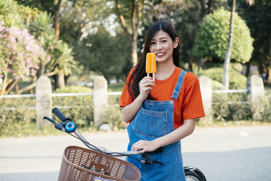 长发女孩穿着橘色t恤和牛仔裤的套头衫吃橘色的冰淇淋，横。