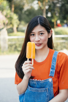 身着橙色t恤和牛仔裤套头衫的长发女孩展示橙色冰淇淋。