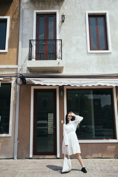 美丽的白衣长发女孩站在阳光下的经典建筑前。